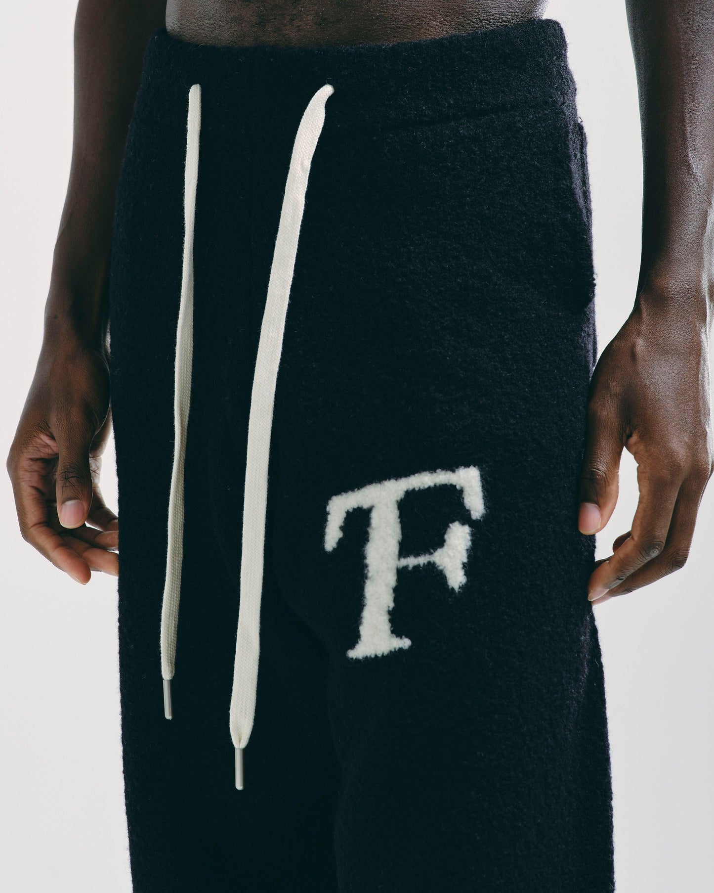 Close-up of men’s black knitted joggers, showing detailed knit fabric and drawstring waistband.