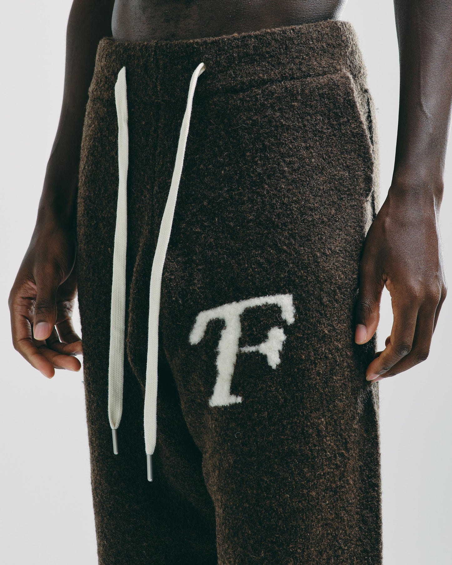 Close-up of men’s mocha brown knitted joggers, showing detailed knit texture and embroidered logo